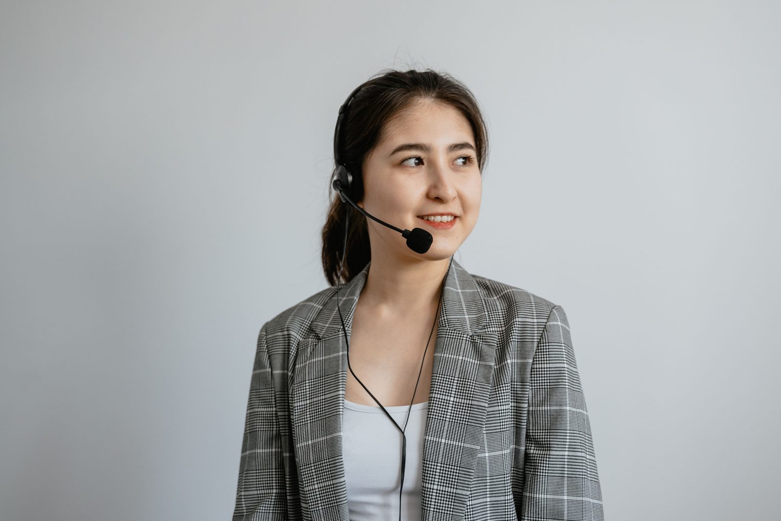 A smiling receptionist wearing a headset against a plain wall