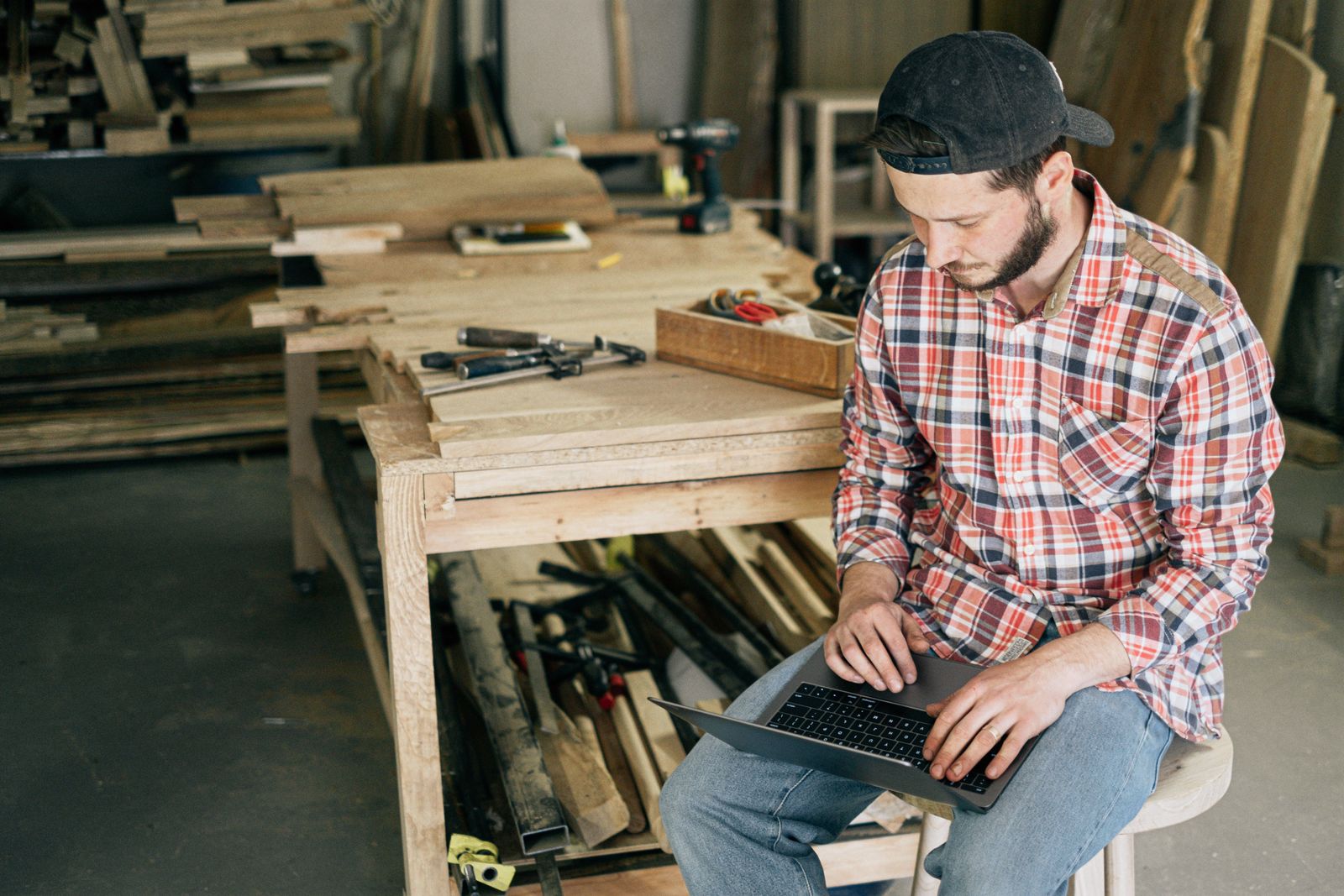 A tradesman in a workshop typing on a laptop