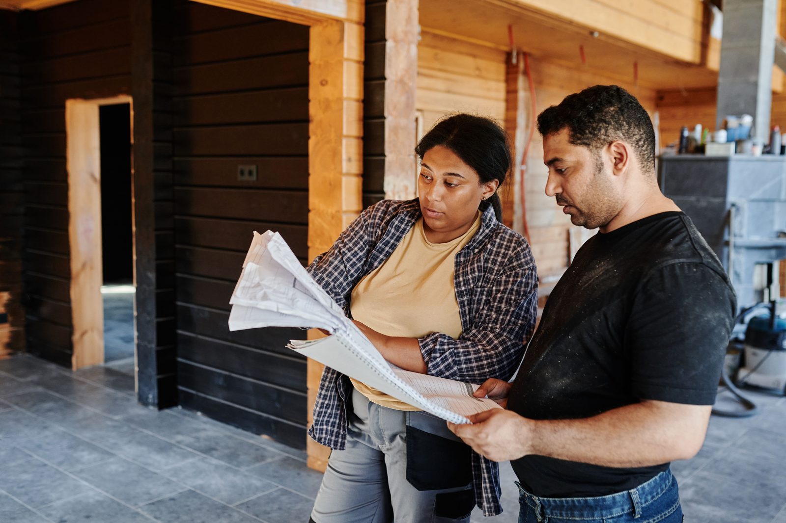 Two workers reading a set of construction plans inside a timber-frame building under construction