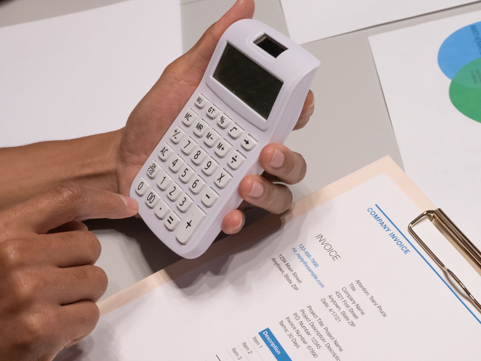 Hands holding a calculator over a printed invoice on a clipboard