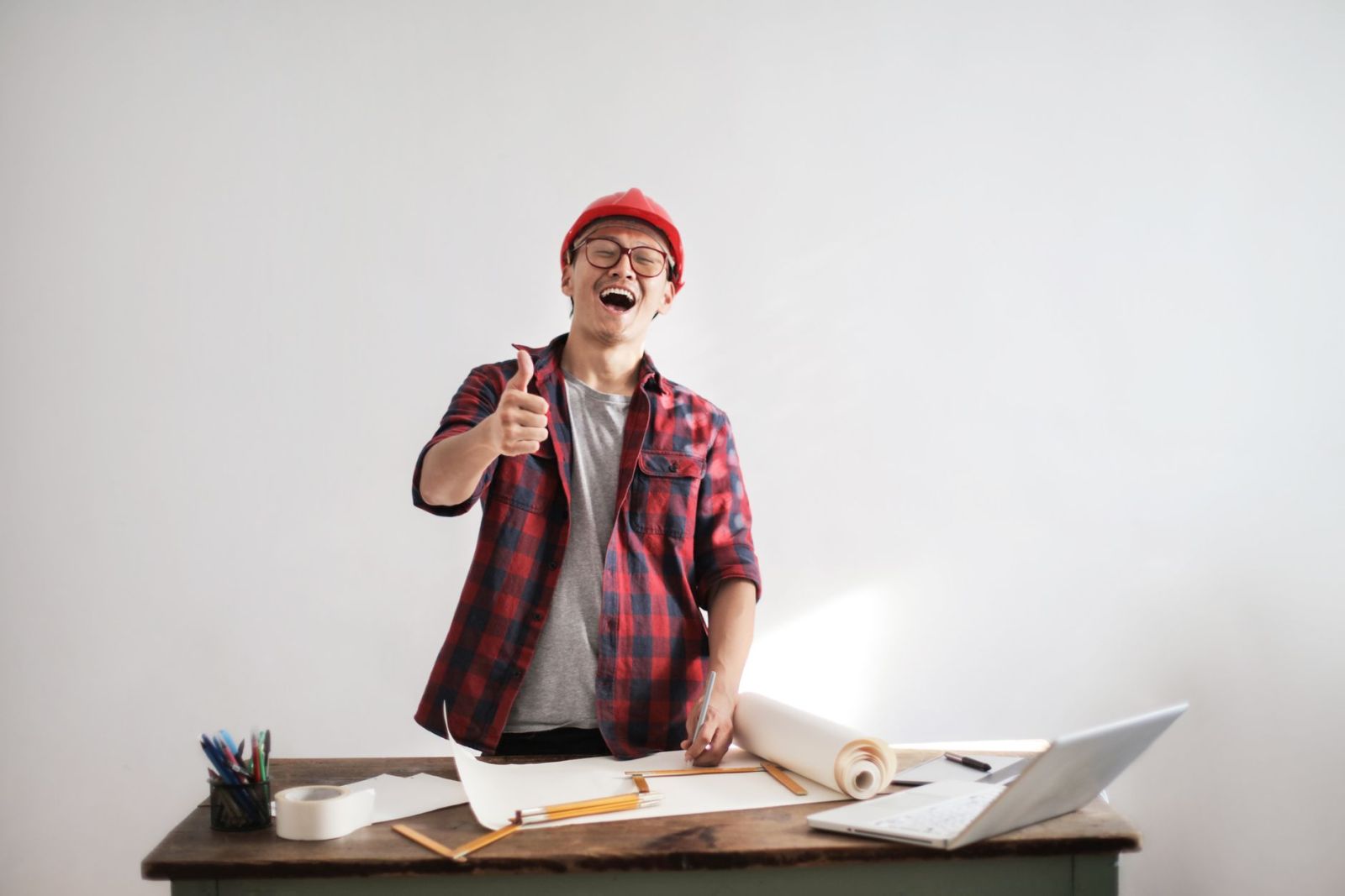 A contractor in a hard hat giving a thumbs up at his desk