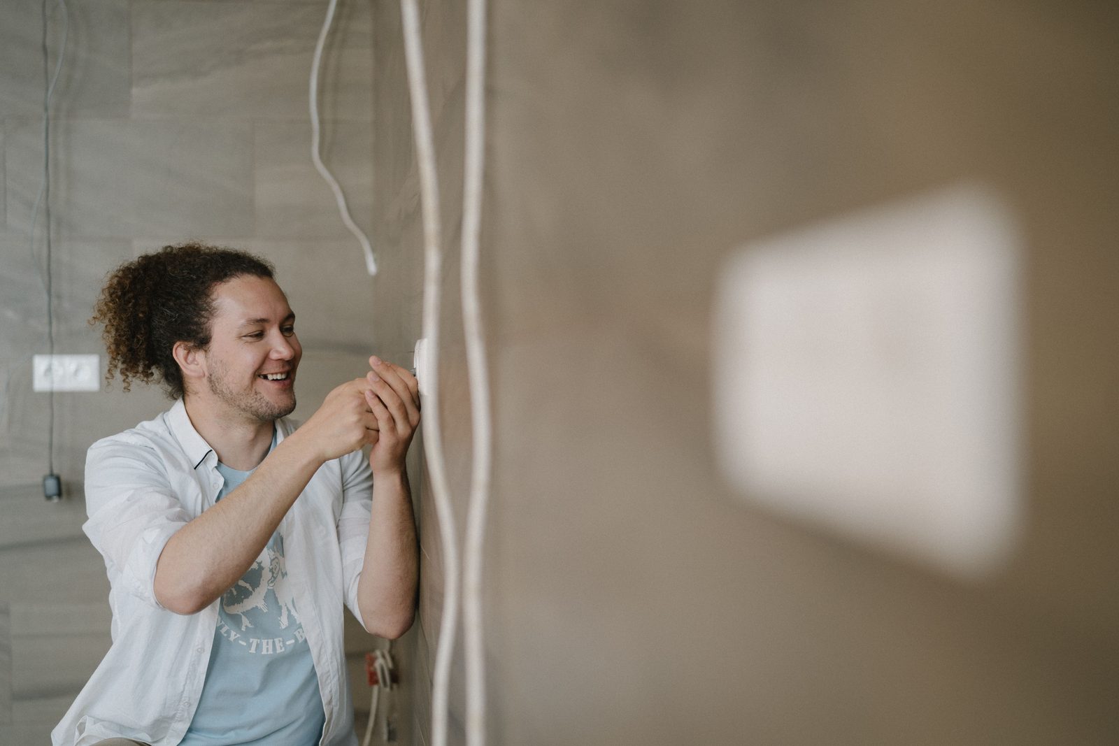 A smiling electrician adjusting a wall outlet during installation work indoors