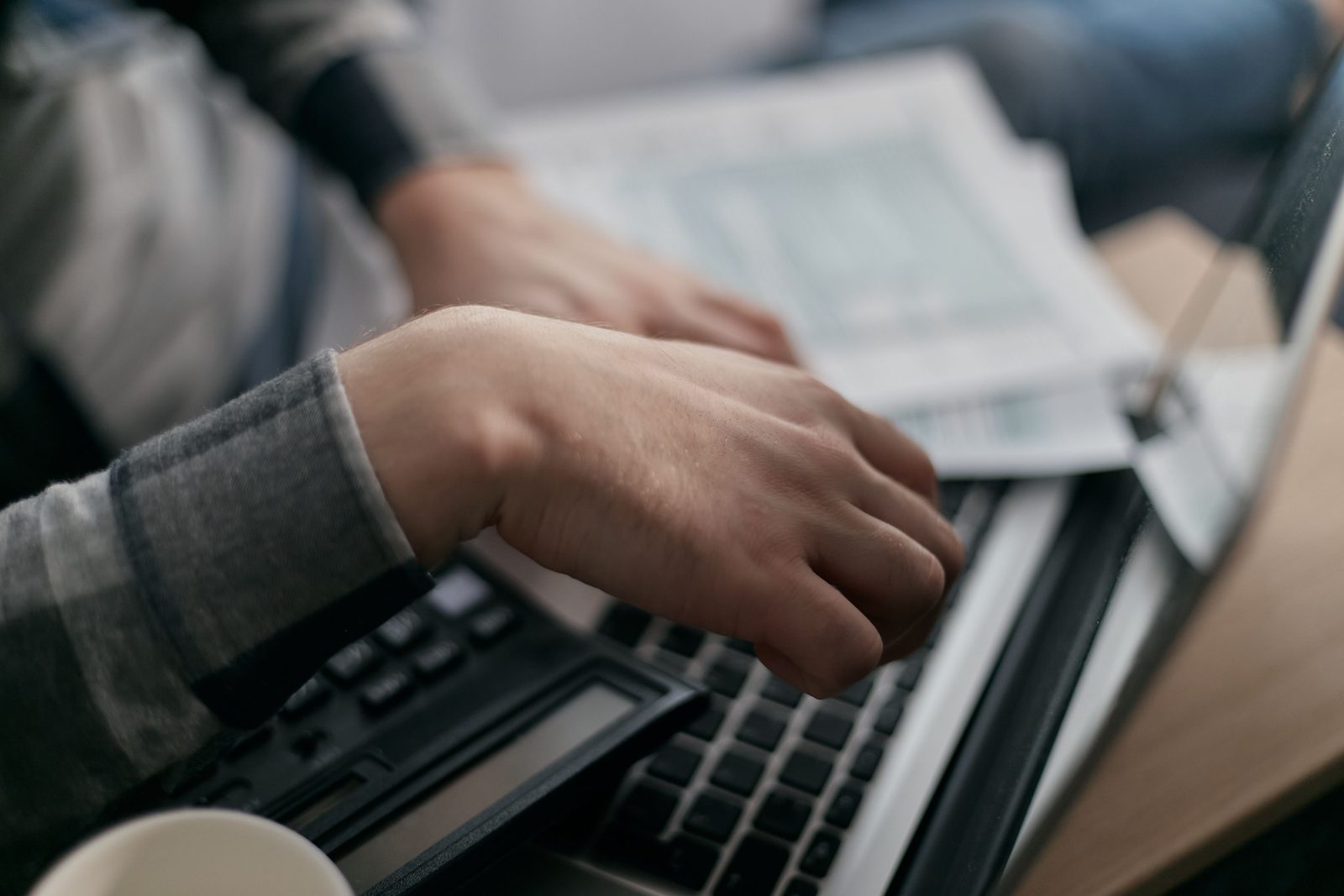 Hands working on a laptop next to printed financial paperwork