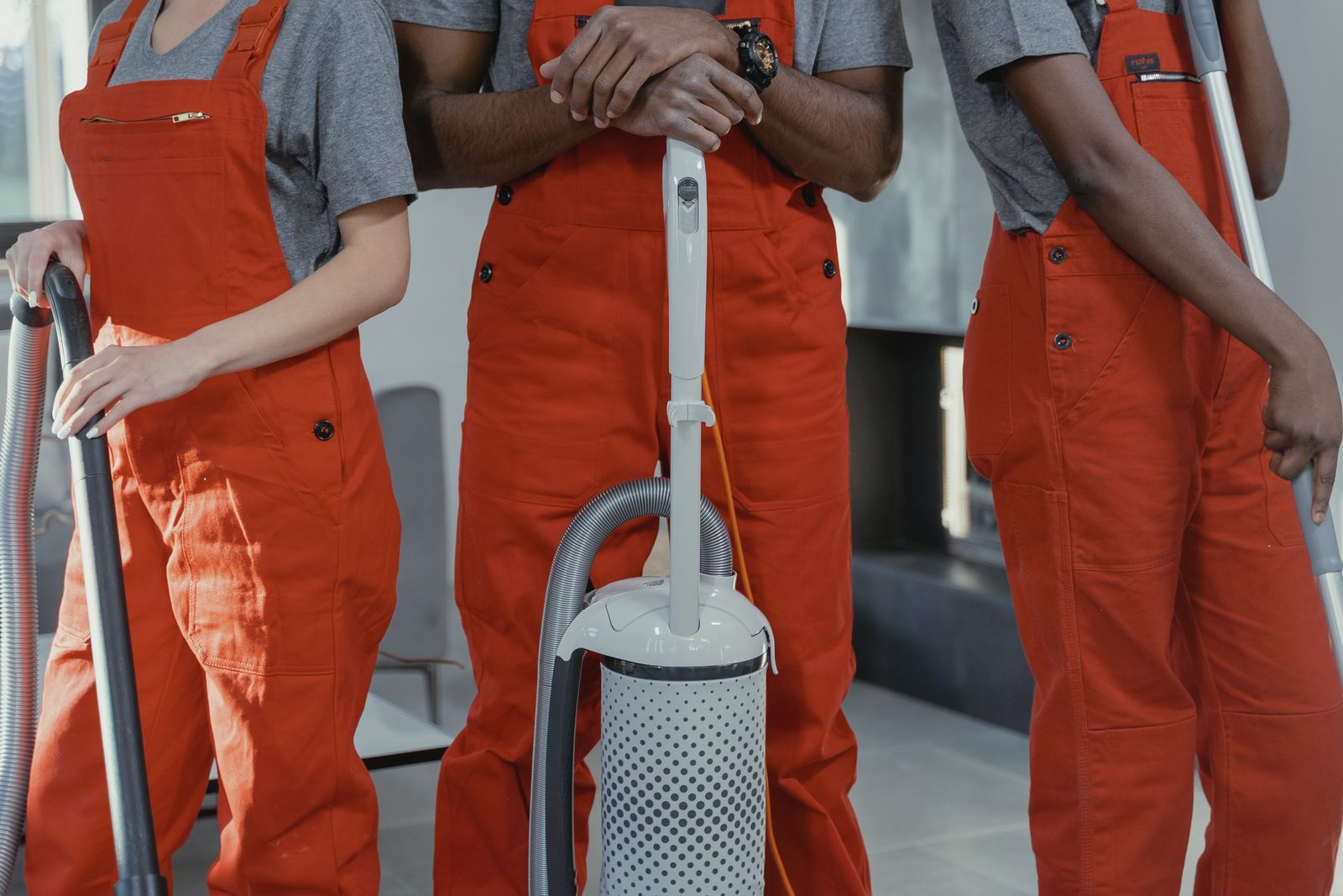 Three cleaners in red overalls standing in a room with vacuum cleaners