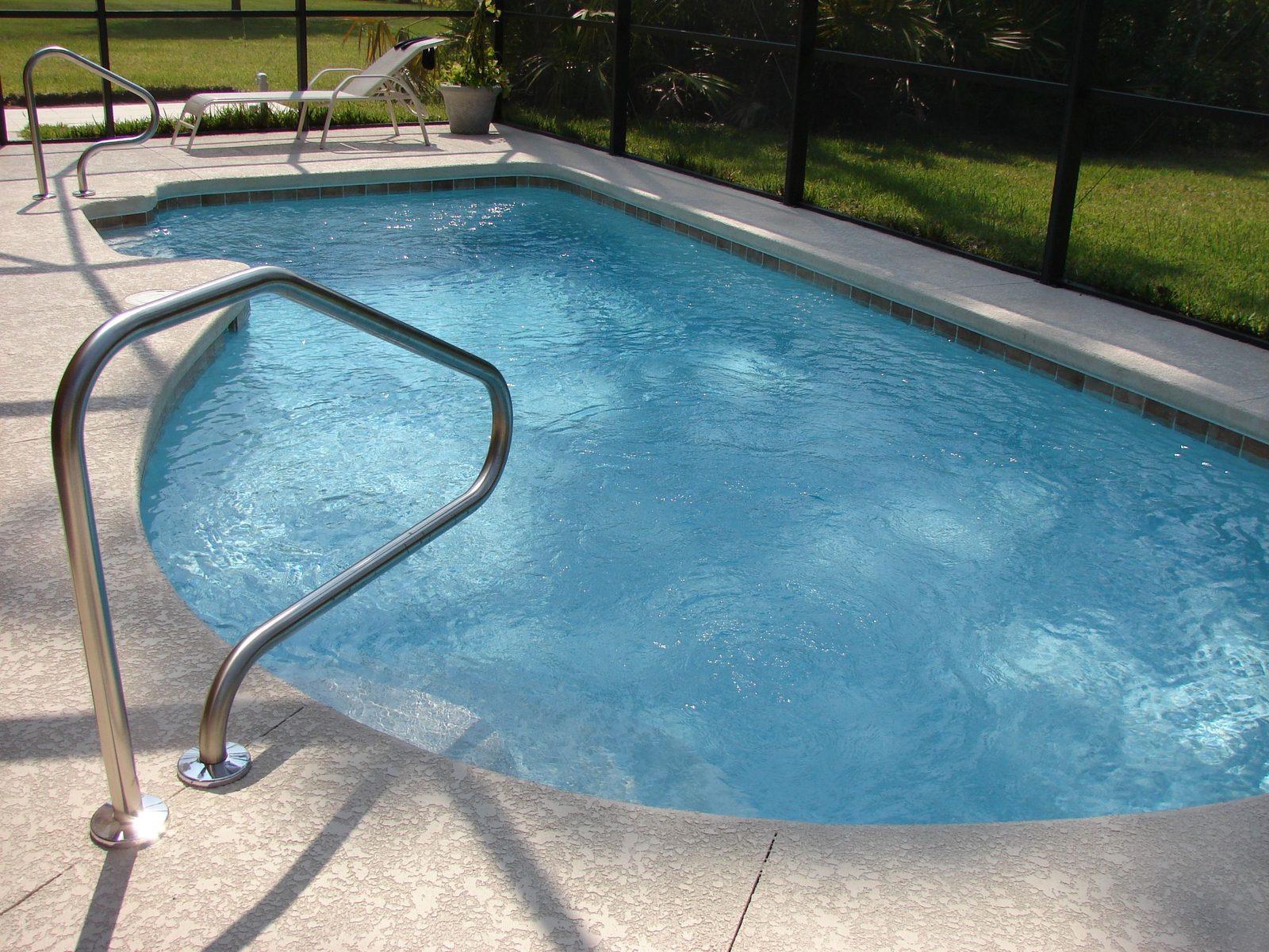 A residential swimming pool with a metal handrail inside a screened pool enclosure