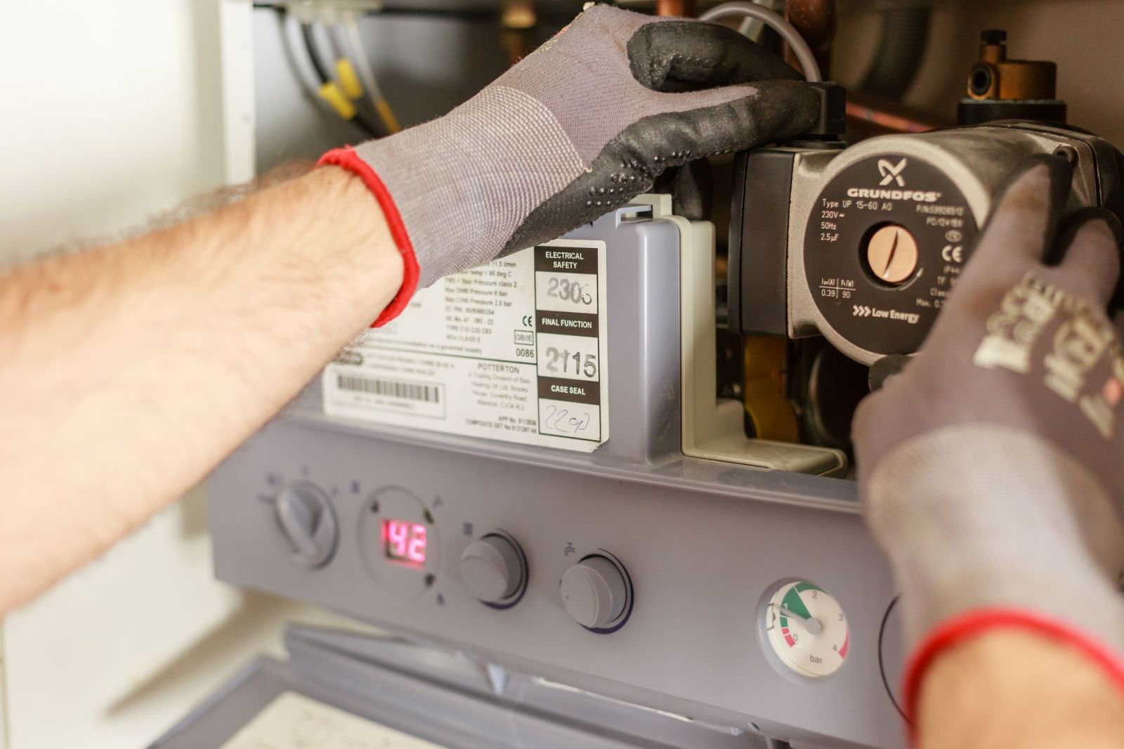 Gloved hands servicing a wall-mounted boiler