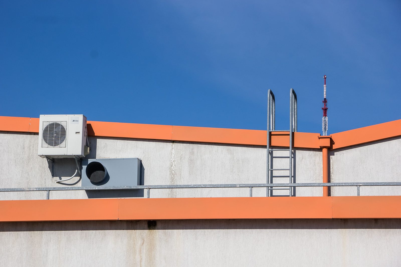 An outdoor air conditioning condenser and an exhaust unit on a commercial rooftop next to a ladder