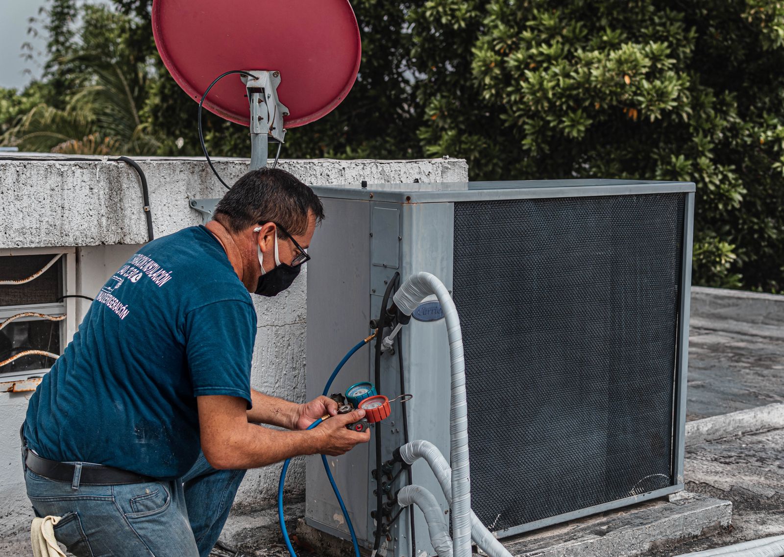 An HVAC technician checking refrigerant pressures with a manifold gauge on a rooftop condensing unit
