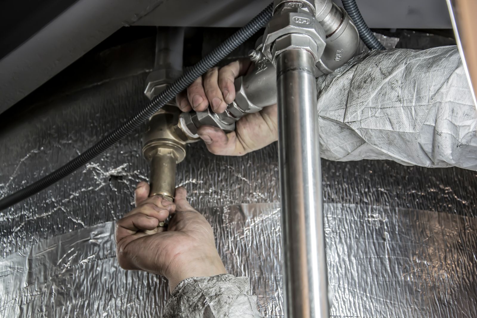 A plumber's hands tightening a brass fitting on a pipe under a sink