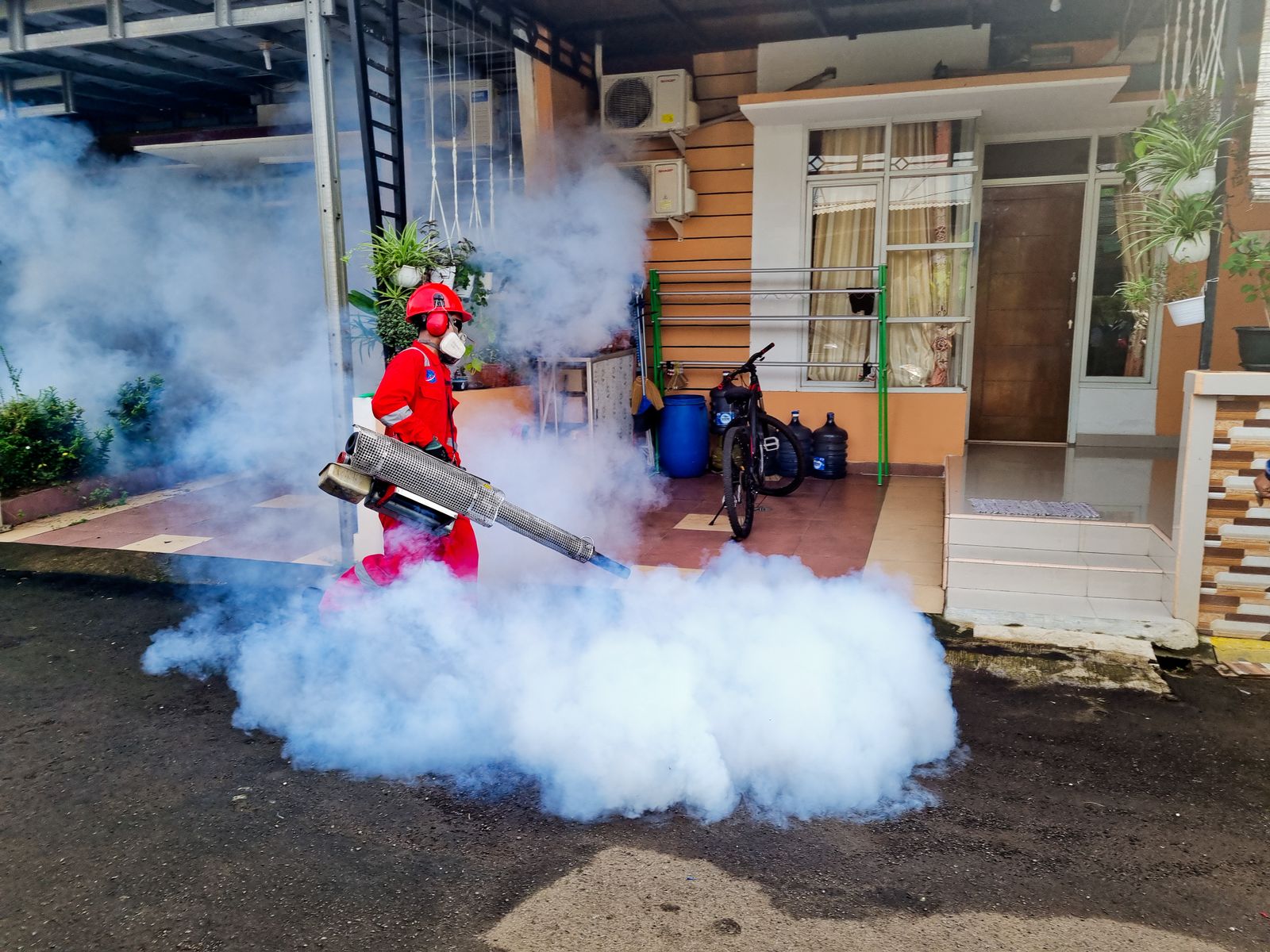 A pest control worker in protective gear fogging outside a house