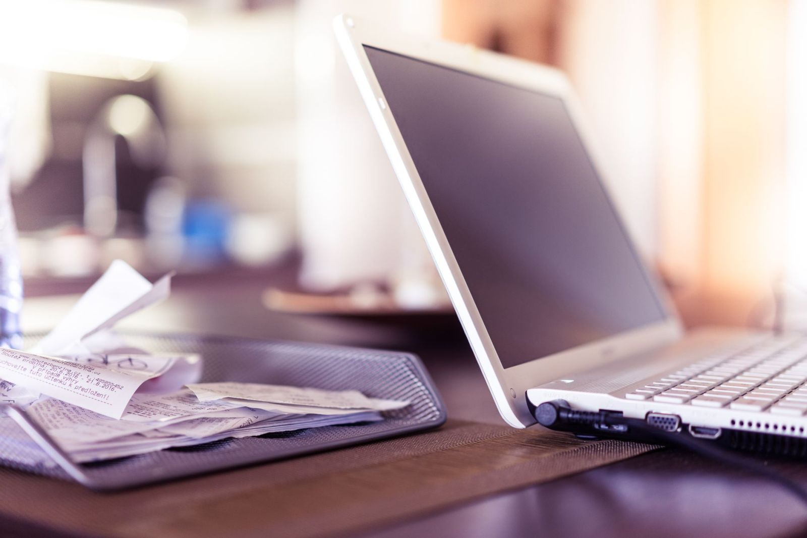 A laptop on a desk next to a tray of paper receipts
