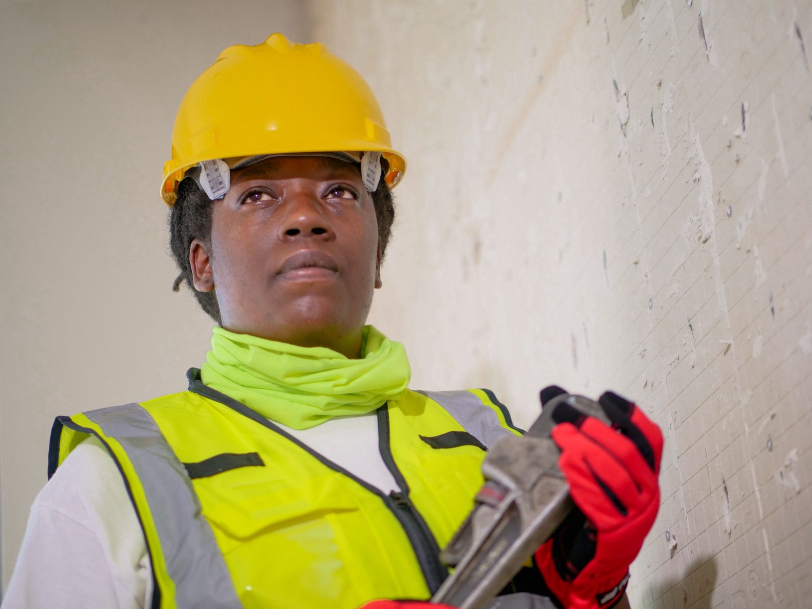 A tradeswoman in a hard hat and high-visibility vest holding a pipe wrench