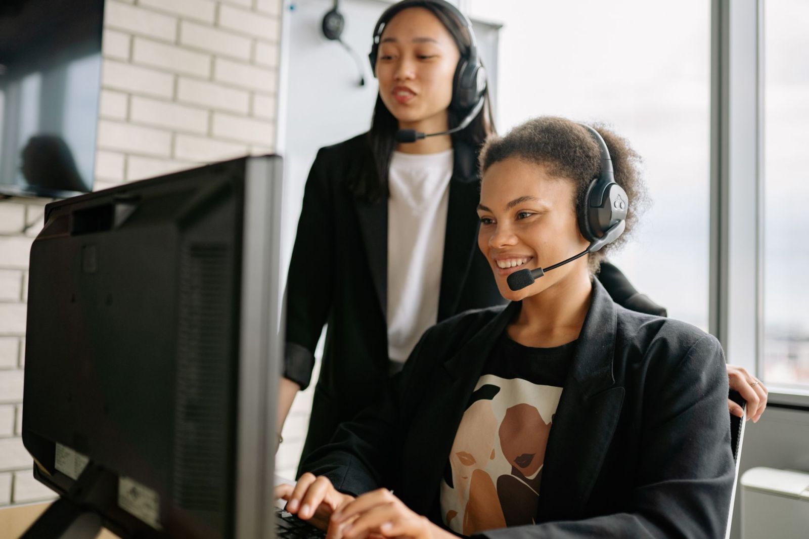 Two office staff with headsets working at a computer